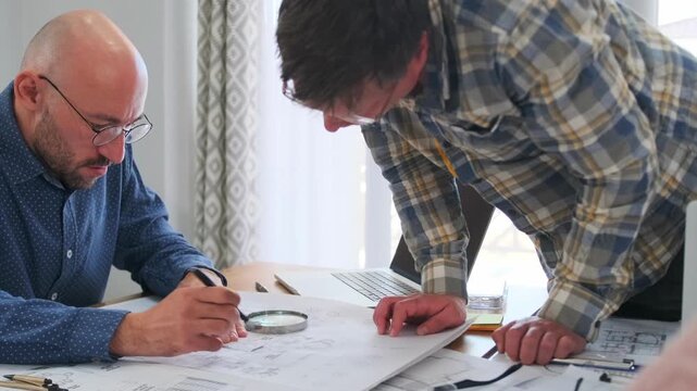 Focused preparation for a construction project. Architect and foreman carefully analyze blueprints with magnifier and ruler, discussing details for creative design and building implementation in a