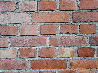 Close-up of weathered red-brown brick wall with staggered joints and gray mortar. Surface shows chips and discoloration, highlighting aged masonry texture and classic construction detail.