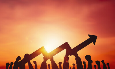 Silhouette of many hands holding a growing arrow symbol on sunset background. Business concept,...