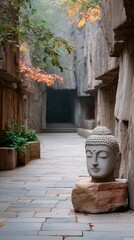 Ancient weathered stone Buddha head sculpture carved into natural rock formation pathway with autumn foliage and misty atmosphere a serene spiritual art form in daylight