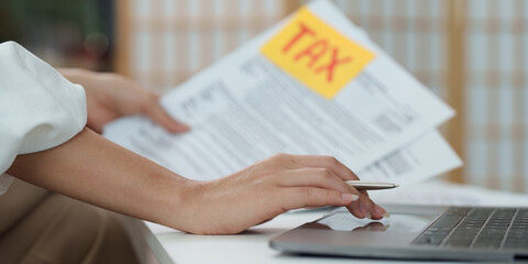 Tax management. Person reviewing tax forms and using laptop for financial calculations.