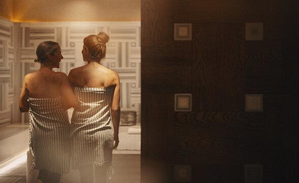 Mature woman and young woman entering a luxury hammam spa together, wrapped in towels, sharing a moment of relaxation and bonding