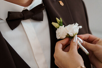 Elegant Groom Boutonniere Pinning: Brown Suit, White Flowers, Formal Wedding Attire, Close-up, Soft Lighting, Stylish Ceremony Detail.