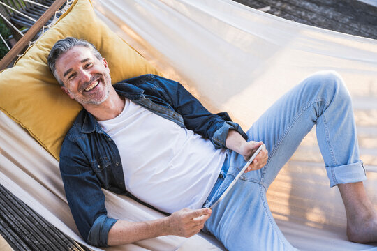 Happy mature man with tablet PC relaxing in hammock - Powered by Adobe