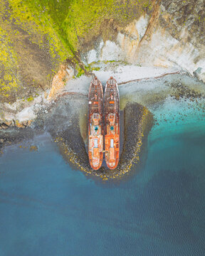 Aerial view of rusty shipwrecks lie stranded on the shore, a stark contrast against the azure waters and verdant cliffs, Beached Whalers Hvalfjrdur, Hvalfjardarsveit, Iceland.
