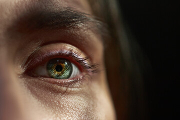 close-up view of a human eye showcases a blend of green and gold hues. light reflects off the...