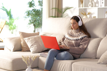 Serious woman in winter at home using laptop wearing headphone