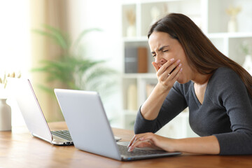 Tired woman using two laptops in a house interior