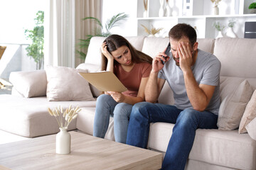 Worried couple reading paper documents calling on phone at home
