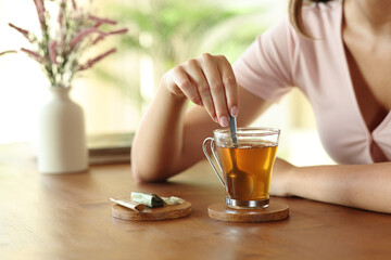 Woman hand stirring tea in a transparent cup at home
