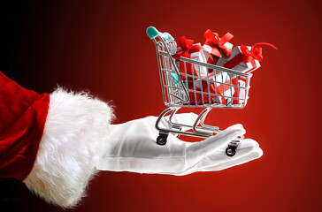 Santa's hand holding shopping cart full of gifts isolated red