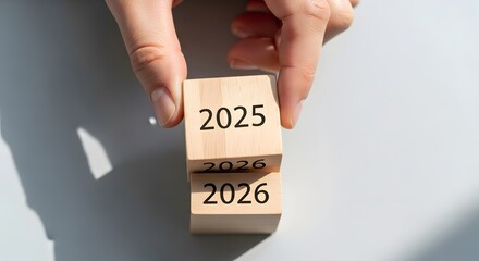Hand flipping wooden blocks from 2025 to 2026, representing the passage of time, new year transitions, future planning, and setting strategic goals for the upcoming period