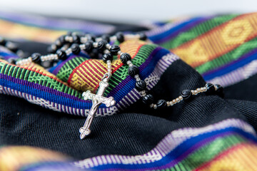 A detailed close-up photo of black rosary beads with a silver crucifix resting on colorful...