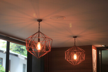 Two modern geometric copper pendant light fixtures hanging from ceiling create warm and inviting glow. stylish interior design element for home decor and decoration