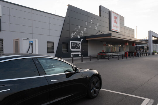 Tychy, Poland - September 26, 2021. A static shot of a solid black Tesla Model 3 dual motor charging at the Kaufland supermarket DC charging station in a sunny autumn day. Selective focus.