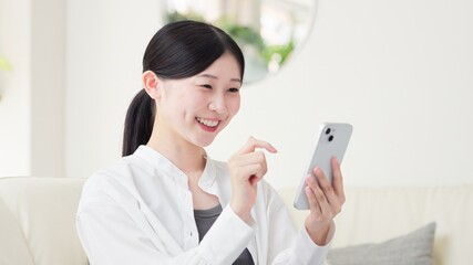 リビングでスマホを操作するアジア人女性 © mapo