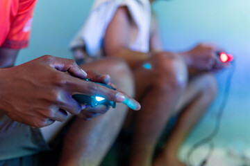 Close-up photo focusing on hands holding controllers while two friends play video games. The...