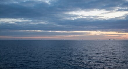 Fototapeta premium Calm ocean horizon with ships near dusk, under a partly cloudy, soft-lit, tranquil sky