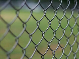 Fototapeta premium Close-Up of Chain Link Fence with Shallow Depth of Field - Metal Wire Mesh Barrier with Blurred Green Background