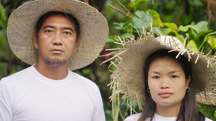 Serious closeup portrait of southeast asian farmers, husband and wife, couple, wearing straw hats