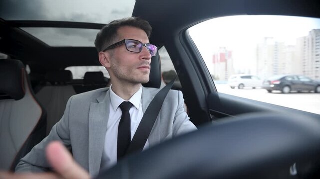 A man in a suit and tie is driving a car with a man in the passenger seat