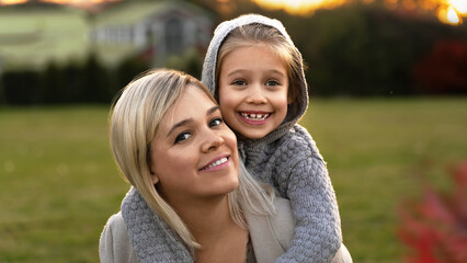 Portrait of happy family fun walk in autumn park at sunset. Mother and little daughter look at...