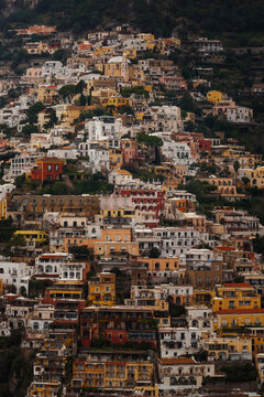 Aerial view of sun-drenched buildings cascade down the hillside, a vibrant tapestry of ochre, terracotta, and white blending into the landscape, Positano, Campania, Italy.