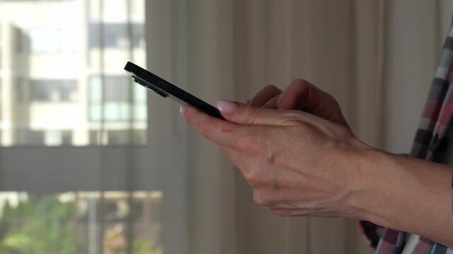 Woman using smartphone pressing fingerers, reading social media internet, typing text or shopping online. A close-up of hands holding a smartphone at home or work.  - Powered by Adobe