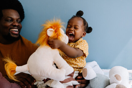 Father and child laugh playing with plush lion