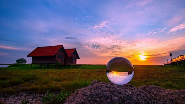 golden sunlight spills across a tranquil lakeside scene. A crystal sphere on the hill captures the world in reverse houses, bridge, and all framing them in vivid colors from the awakening sky.