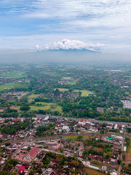 Aerial view of Prambanan Temple and the distant volcano shrouded in mist, a tapestry of green fields and terracotta roofs, Yogyakarta, Daerah Istimewa Yogyakarta, Indonesia.