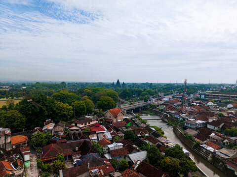Aerial view of terracotta rooftops nestled beside the snaking river, crossed by a bridge amidst lush greenery, Jalan Raya Solo - Yogyakarta, Yogyakarta, Daerah Istimewa Yogyakarta, Indonesia.