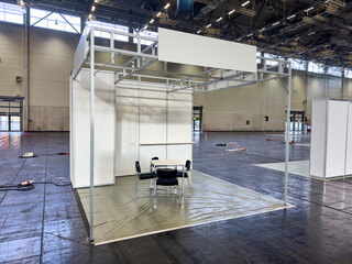 Weisser leerer Messestand in Messehalle mit schwarzen Stühlen und einem Tisch