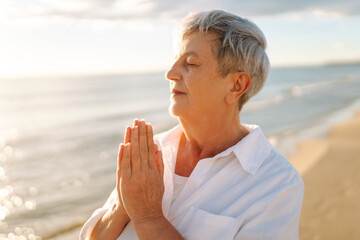 An older woman with gray hair walks along a sunlit sandy beach. The elderly woman enjoys the seascape, feeling the freedom of dawn. Concept of a happy retirement, nature.