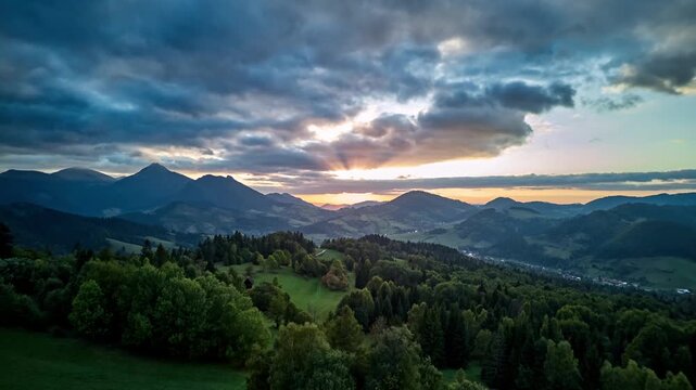Aerial hyperlapse showing forward motion over green mountain valley at sunset with dramatic clouds and sun rays