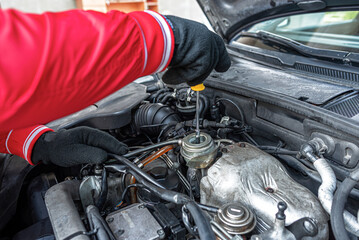 A mechanic wearing gloves performs maintenance on a car engine using tools under the vehicle hood...