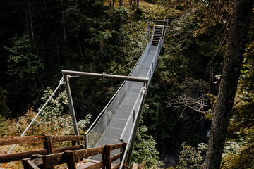 Metal suspension bridge in the Alps near Namlos, Tyrol – hiking trail through dense mountain...