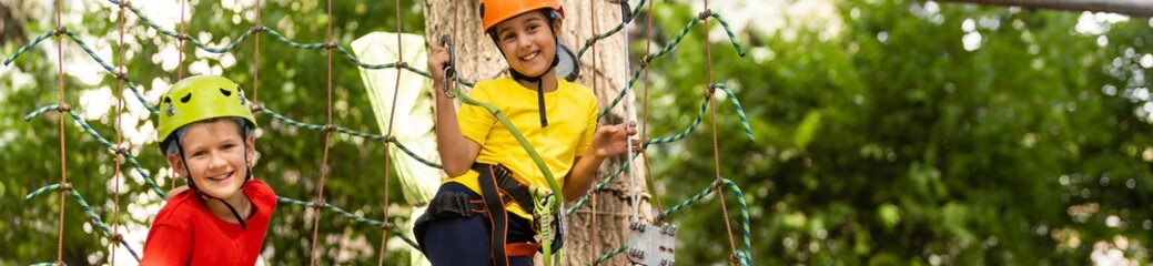 two friends in a helmet, T-shirt and shorts afraid and climbs in a rope park at altitude. safety of...