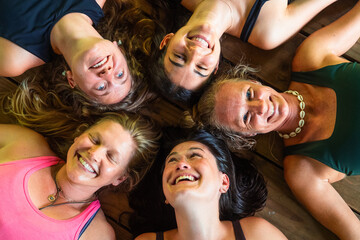 Women lying in circle smiling on wooden floor.