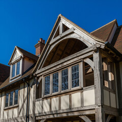 Facade of traditional English Tudor-style home with exposed oak timber frame and gabled roof. Classic half-timbered architecture. Luxury real estate.