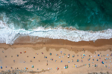 Overhead drone shot of anonymous tourist and colorful parasols on sandy seashore, showing people enjoying summer vacations at beach during sunny day 
