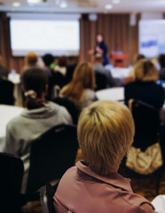 Obraz premium Female audience at the symposyum meeting, participants attendees in conference room hall listens to lecturer, group of women on a medical congress together listen to speaker on a stage at master-class