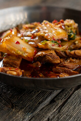 Sichuan lamb ribs with Chinese cabbage. Meat in an iron bowl on a wooden background. Chinese cuisine. Food concepts.