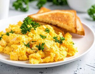 Fluffy scrambled eggs served with toasted bread and garnished with fresh parsley on a white plate, perfect for a healthy breakfast.
