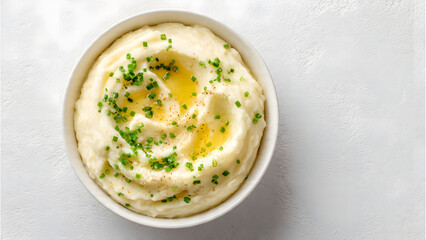 A top-down view of a white bowl filled with smooth and creamy mashed potatoes. In the center, a pat of melting butter creates a golden pool, garnished with finely chopped scallions.