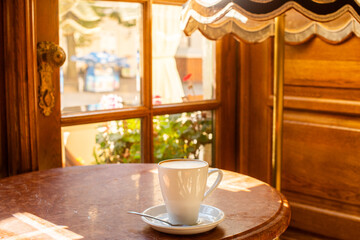 Cup of coffee on a wooden table by the window in a cozy café. Warm morning sunlight creates a peaceful atmosphere — perfect for relaxation, comfort, and slow living moments.