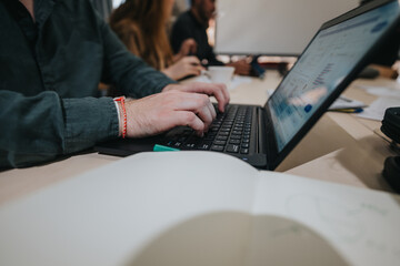 A close-up of hands typing on a laptop keyboard during a collaborative team discussion, symbolizing productivity, teamwork, and office tasks.