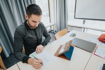 A man works diligently at a desk in an office, surrounded by documents and technology. He appears...