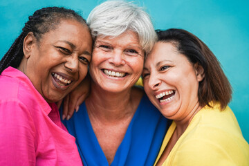 Multiracial senior women having fun hugging together outdoor - Friendship and joyful lifestyle concept - Main focus on african female face
