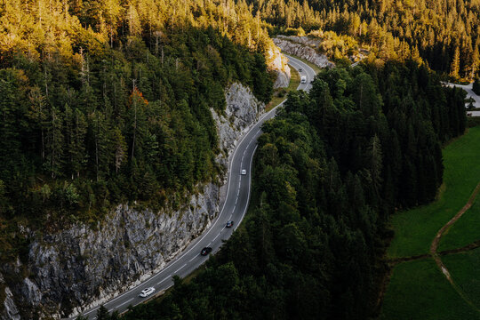 Aerial top down view of cars driving on a winding alpine mountain road through a green forest in Tyrol, Austria